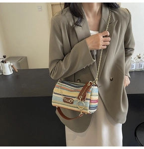 Detail of colorful woven cylinder bag with leather handles and gold chain strap on a model