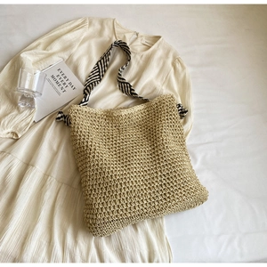 Detail of woven straw tote bag with black and white wavy shoulder strap on white dress