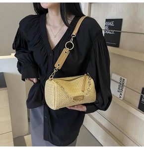 Close-up of straw woven cylindrical bag with leather strap and decorative metal chain