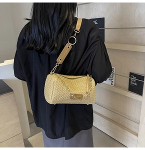Detail of woven straw bucket bag with leather strap and chain shown on model