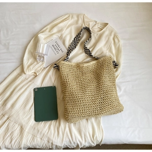 Close-up of beige woven tote bag with a striped strap on minimalist cream background