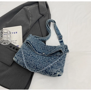 Dettaglio macro del denim trapuntato e della catena argento su una borsa blu