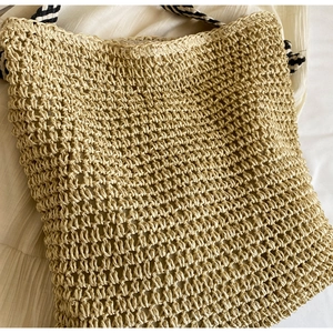 Detail of hand-woven straw tote bag featuring contrast black and white striped handles