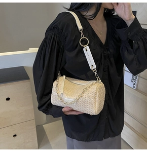 Detail of woven straw cylinder bag with gold chain and logo charm worn by a model