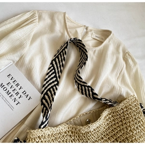 Detail of a creamy pleated shirt paired with a woven straw tote and striped straps