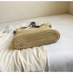 Detail of large straw tote bag featuring beige weave and striped ribbon shoulder straps