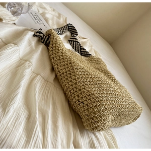 Detail of hand-woven straw tote featuring black and white striped shoulder strap and texture