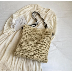 Detail of beige woven straw tote bag with stylish black and white striped shoulder strap