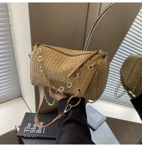 Detail of woven straw cylinder bag featuring decorative gold flower chain and leather strap