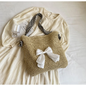Detail of straw tote bag with a white fabric bow and geometric patterned shoulder strap
