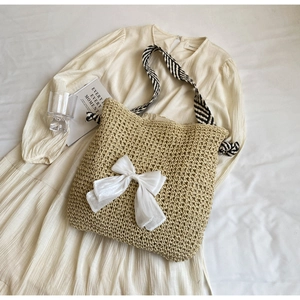 Detail of straw woven tote bag featuring a white silk bow and striped shoulder strap