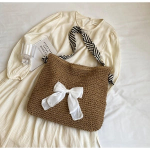 Detail of straw tote bag with white bow and striped handle on lifestyle background