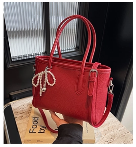 Detail of red lychee grain tote bag featuring a pearl bow charm and detachable strap