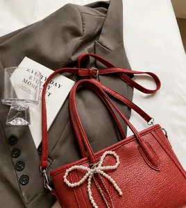 Close-up of red litchi texture tote bag with pearl bow charm on a stylish blazer