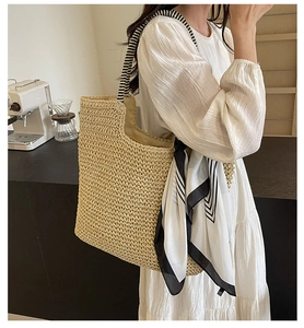 Detail of woven straw tote bag with striped handles and decorative scarf in a cafe setting
