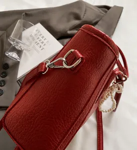 Detail of red synthetic leather tote bag with lychee texture and pearl charm