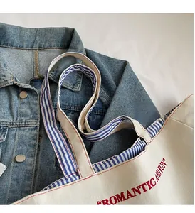 Detail of canvas tote bag handle with blue striped lining and red text embroidery