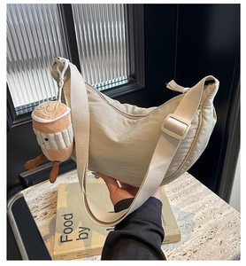 Close-up of beige nylon crescent bag with adjustable strap and coffee cup plush charm