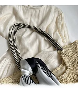 Detail showing handwoven straw tote with black and white striped rope handles and silk scarf
