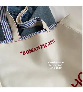 Detail of soft fabric texture and red letter embroidery on cream canvas tote bag