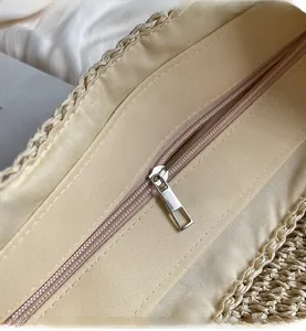 Detail of smooth metal zipper closure on large beige straw tote bag with fabric lining