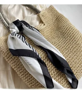 Detail of straw tote bag featuring black and white geometric scarf decoration on handle