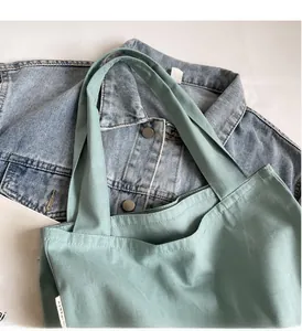 Détail d'un grand sac cabas en toile vert menthe posé sur une veste en jean