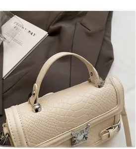 Detail of cream crocodile embossed texture and metallic eagle clasp on a handbag