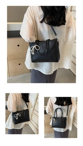 Detail of black pebbled leather tote bag with elegant pearl bow charm and shoulder strap