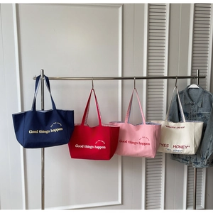 Detail view of four canvas tote bags in navy, red, pink, and beige with slogan prints