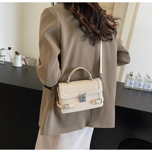 Detail of cream crossbody bag with croc texture and metal butterfly buckle on a cafe counter