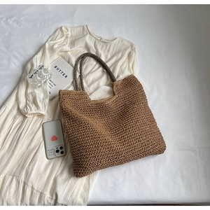 Flat lay of a woven straw tote bag with black and white striped rope handles on a white dress