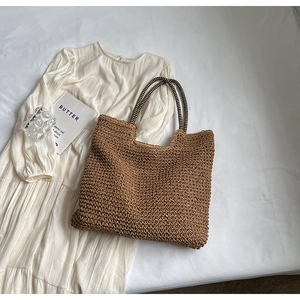 Close-up of brown straw tote bag featuring stylish black and white striped handles