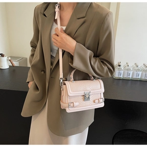 Detail of pink snakeskin embossed crossbody bag with heart clasp worn with olive suit