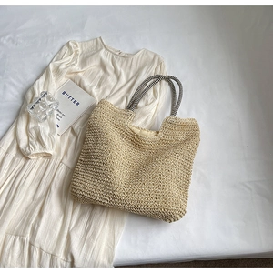 Detail of beige straw tote bag with black and white striped handles on white fabric