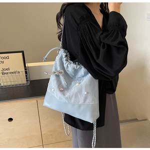 Detail of light blue bucket bag featuring pearl charms and a silver bow pendant