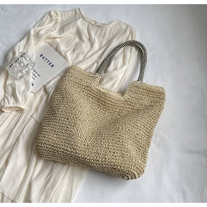 Detail of hand-woven straw tote bag with black and white striped rope handles