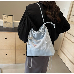 Close-up of light blue drawstring bucket bag with pearl decor and crystal bow charm