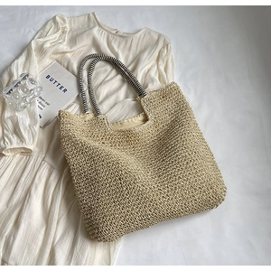 Detail of hand-woven straw tote with black and white striped handles on a neutral surface