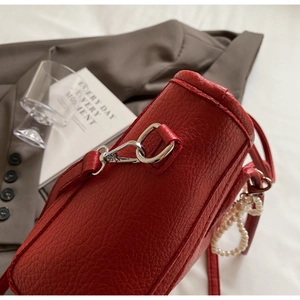Detailed macro view of red pebbled leather bag with pearl charm and silver hook