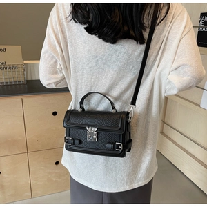 Rear view of a black snakeskin-textured small square bag worn crossbody on a woman