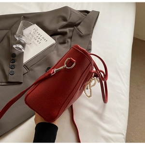 Close-up of deep red pebbled leather tote bag with elegant pearl chain accessory