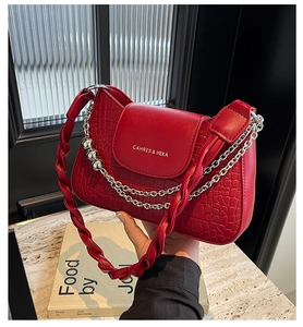 Detail view of red shoulder bag with crocodile texture, silver chain, and top handle