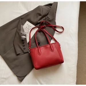 Detail of red lychee textured tote bag styled on business attire with metal hardware
