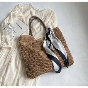 Detail of a large woven straw tote with striped handles and decorative silk scarf accessory