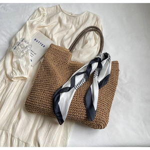 Detail of hand-woven straw tote with striped handles and decorative geometric scarf