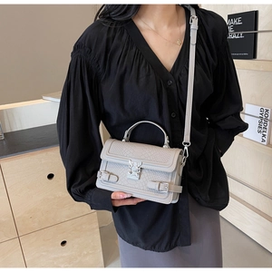 Detail of light gray embossed leather handbag with adjustable strap and metal clasp