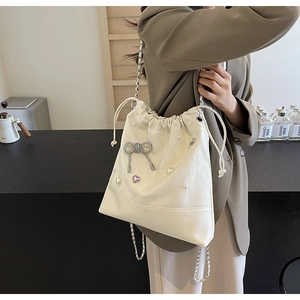 Close-up of cream bucket bag featuring pearl decor, silver bow and chain strap