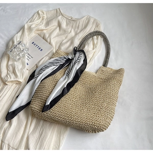Detail of woven straw tote bag featuring striped handles and decorative floral silk scarf