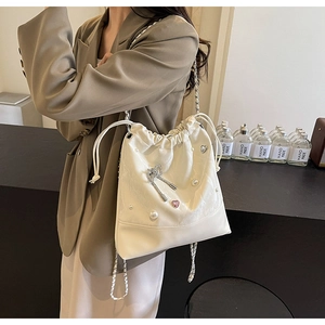 Detail of cream bucket bag featuring pearl accents, diamond bow, and silver chain strap